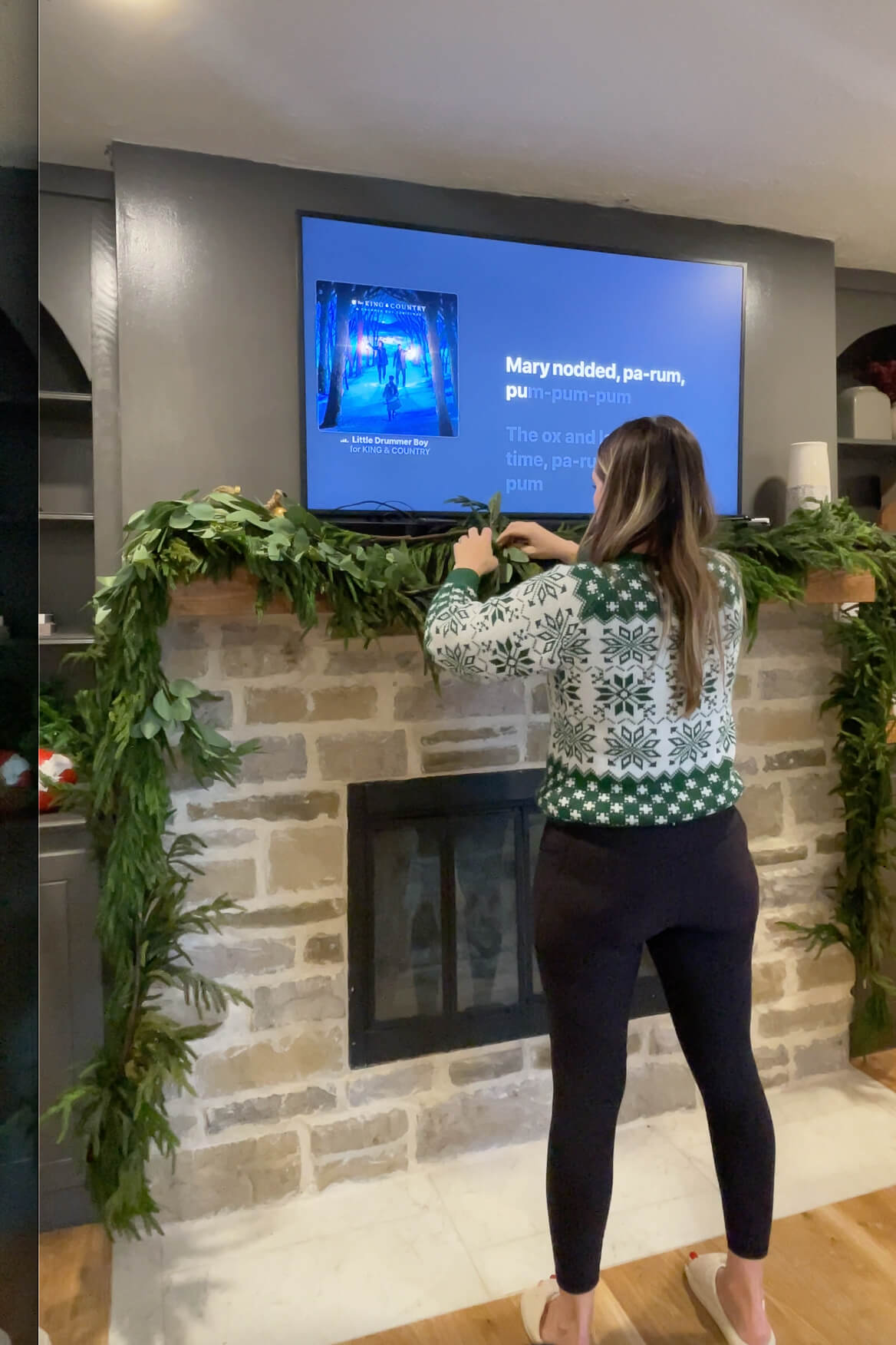 Decorating a fireplace mantel for Christmas using realistic-looking pine garland.